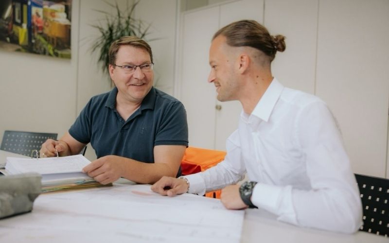 Zwei Mitarbeiter der Klefenz GmbH im Planungsgespräch mit Bauunterlagen im Büro.