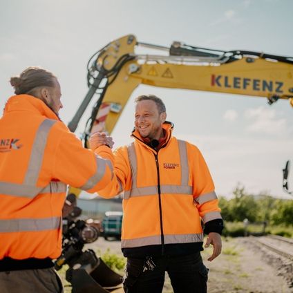 Zwei Mitarbeiter der Klefenz GmbH begrüßen sich auf einer Baustelle vor einem Bagger.