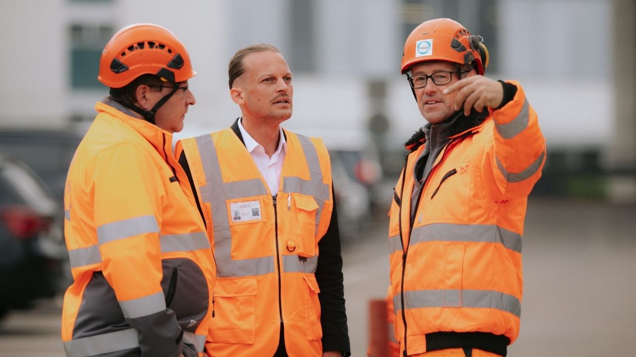 Baustellenbesprechung mit drei Fachkräften in Warnkleidung bei der Abstimmung eines Bauprojekts.