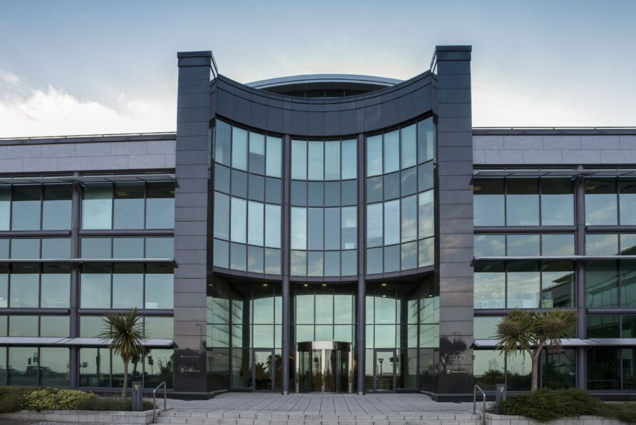Modern office building with large reflective glass windows and a curved entrance flanked by two pillars.
