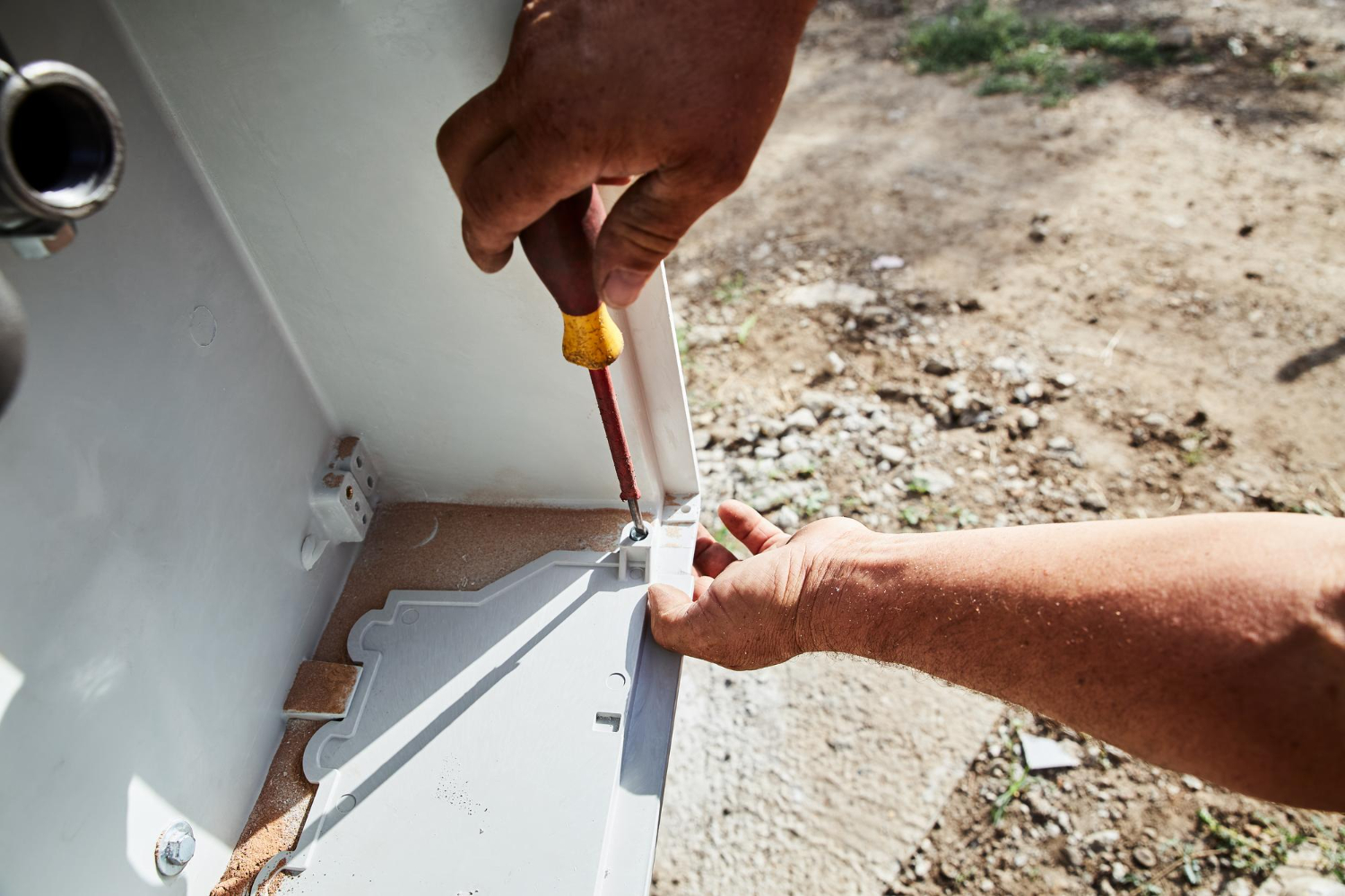 Hands using a screwdriver to tighten a screw inside a metal enclosure outdoors.