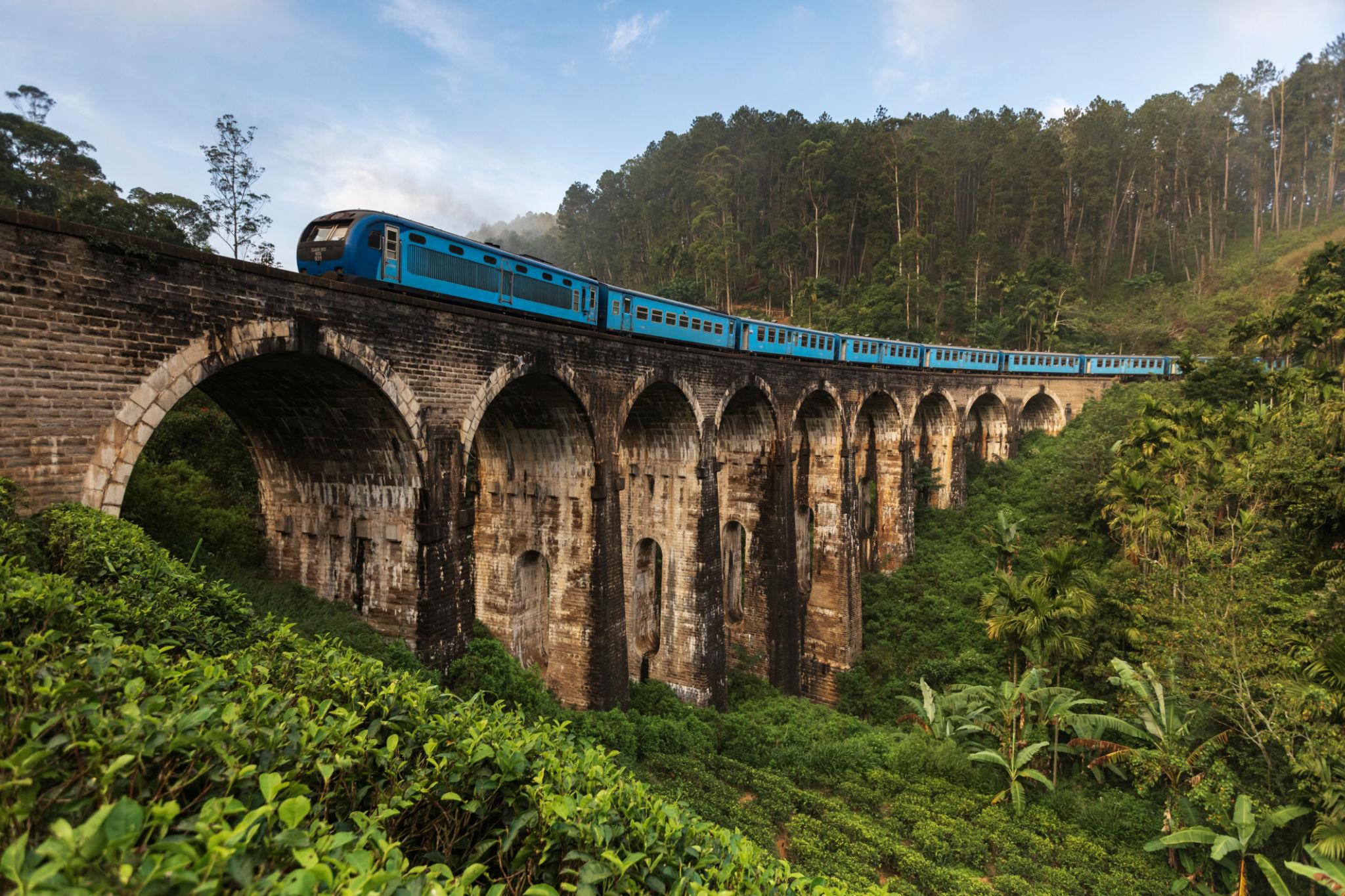 A side view of the Nine Arch bridge Ella with a blue train on it.