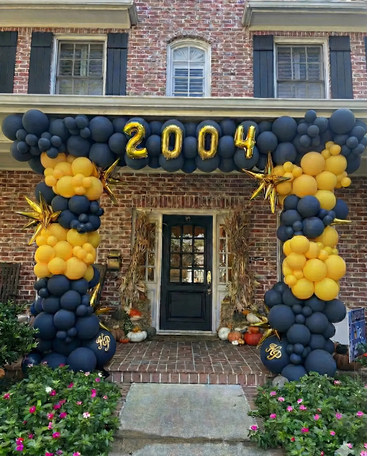 House entrance decorated with black and gold balloon arch displaying the number 2004 and autumn-themed decor around the door Highland Park Scots high school reunion in Dallas.