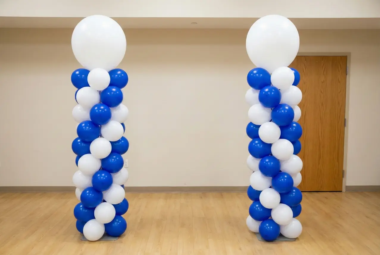 Two vertical balloon columns made of alternating blue and white balloons with a large white balloon on top, standing indoors on a wooden floor in Dallas.