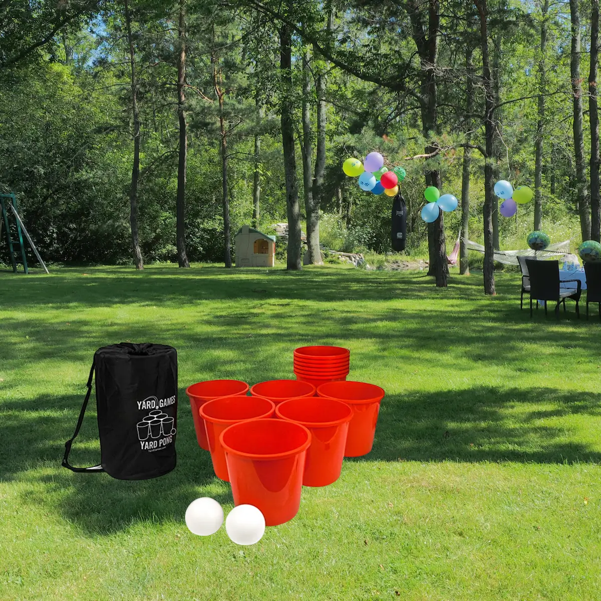 Yard pong game setup with red cups and white ping pong balls on green grass in a wooded outdoor area.