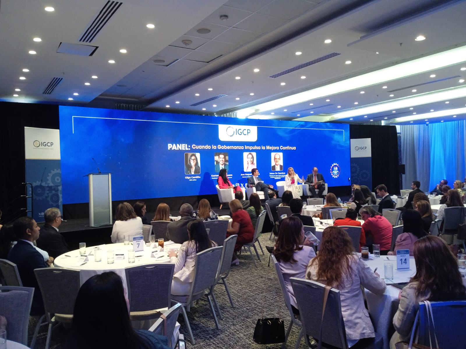 Pantalla LED de fondo de escenario en un panel corporativo con audiencia en mesas redondas