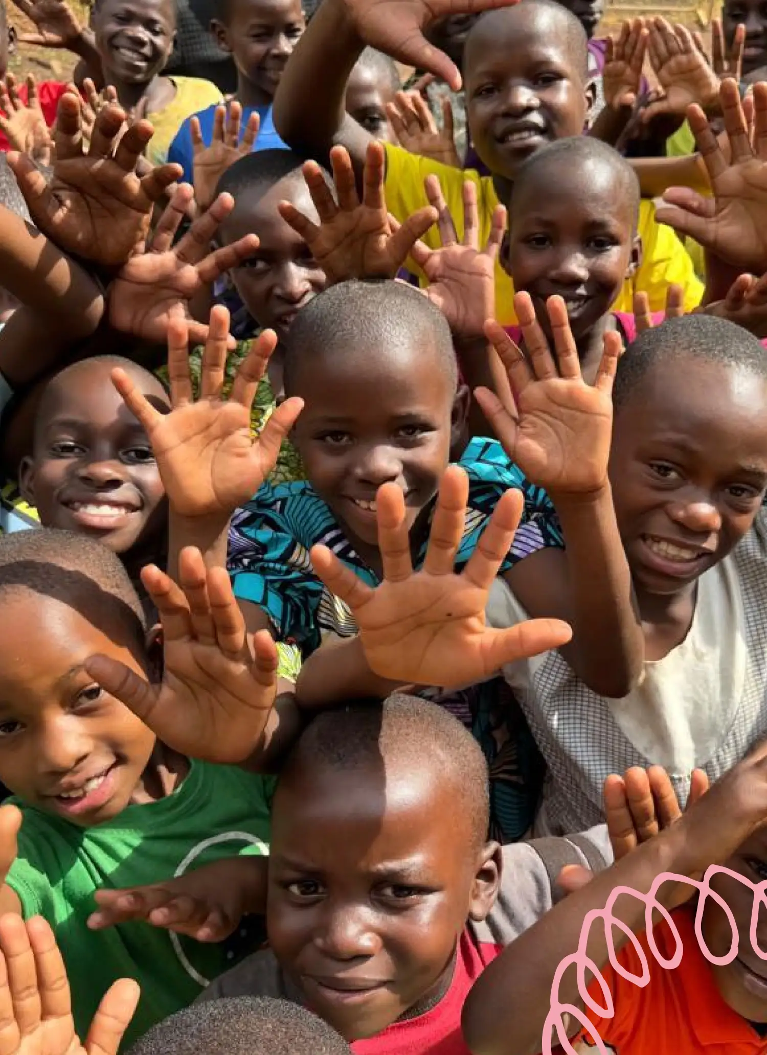 Group of smiling children raising their hands toward the camera outdoors.