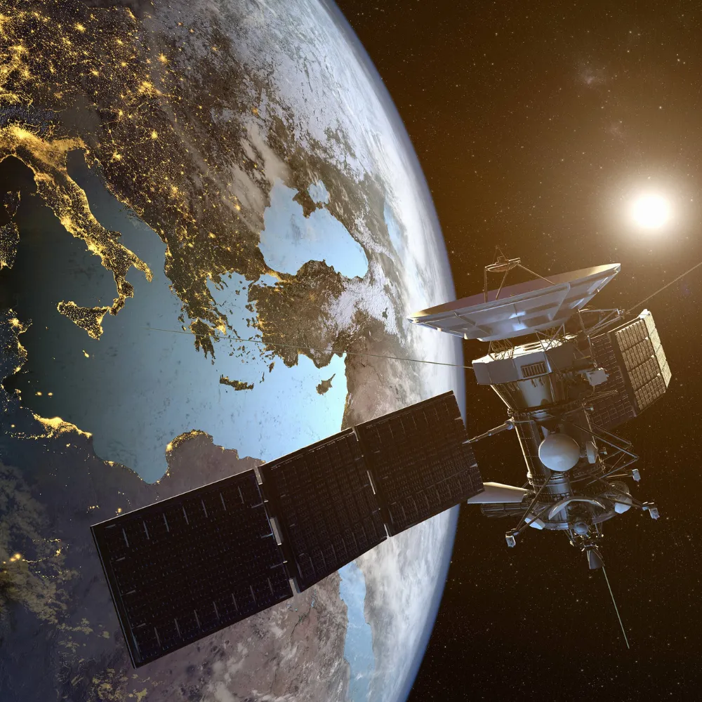 Satellite with solar panels orbiting Earth over the Mediterranean Sea with city lights visible at night.