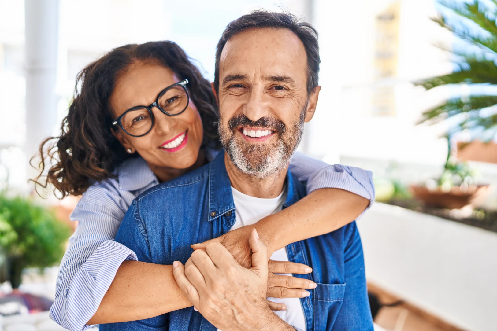 Smiling middle-aged couple hugging closely with woman wearing glasses and man in denim shirt.