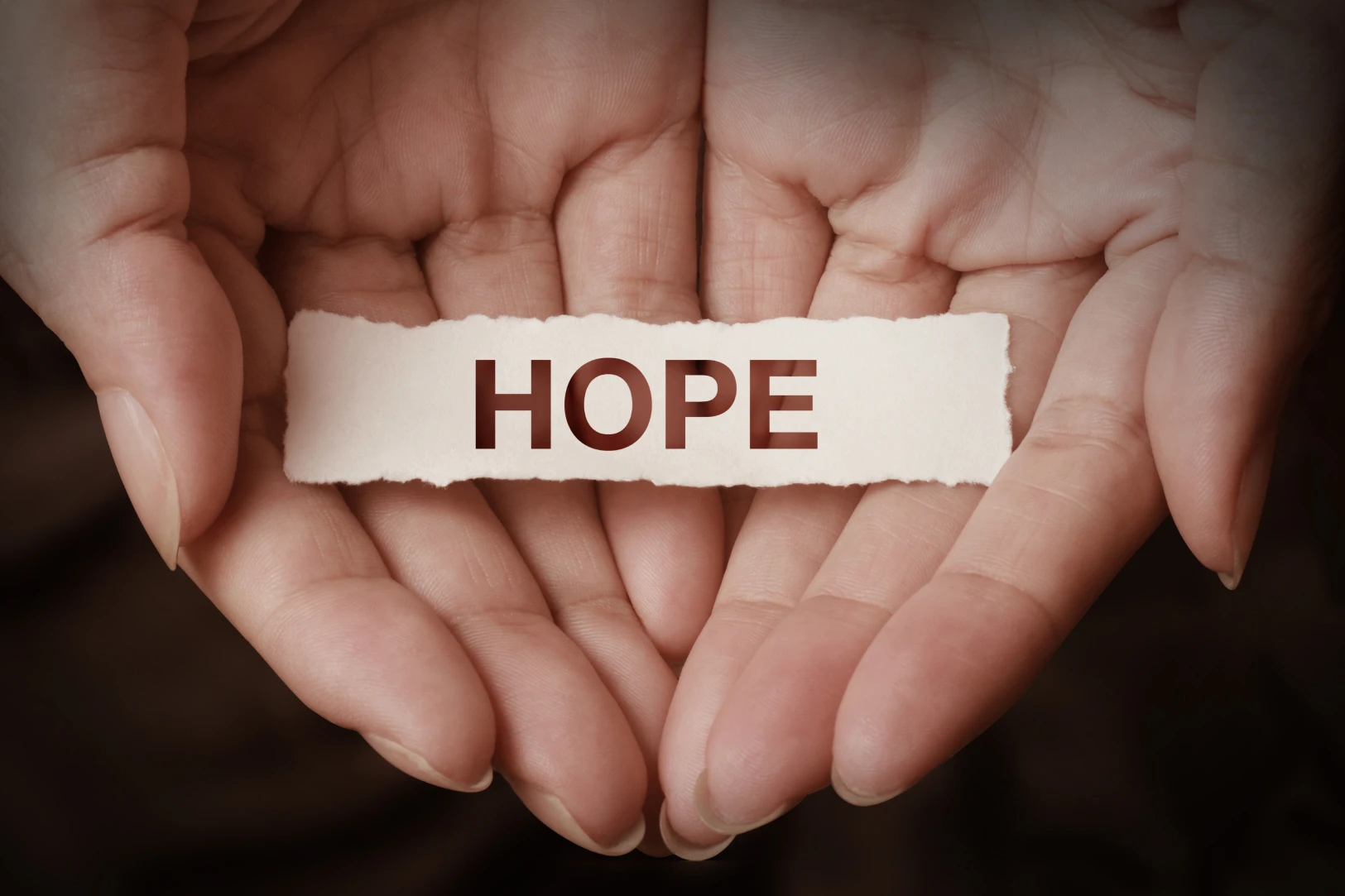 Hands gently holding a piece of torn paper with the word 'HOPE' printed on it.