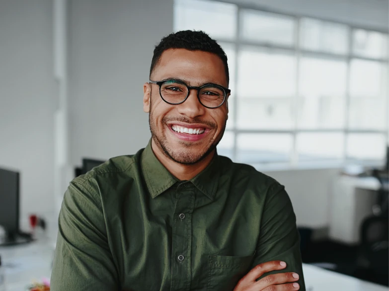 Smiling man with glasses wearing a green shirt in a bright office setting.