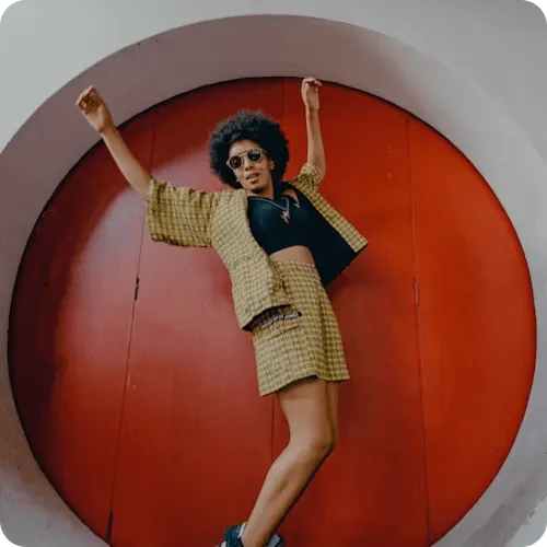 Image of a woman wearing a yellow skirt and jacket stands confidently in front of a circular door, showcasing her vibrant style.