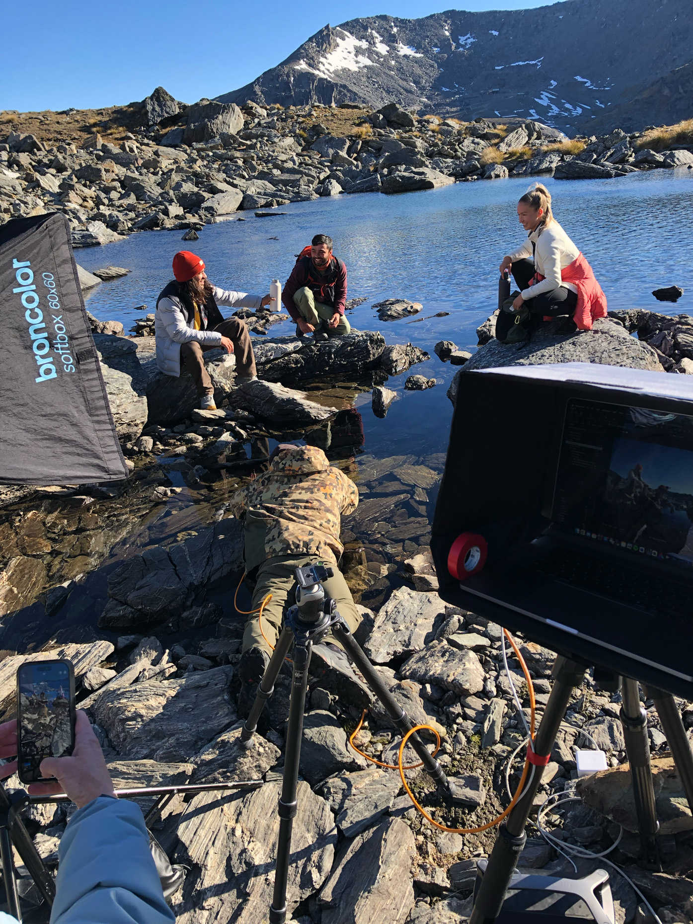 Team with commercial photographer working in an alpine setting, with a lake and mountains with snow behind them in Queenstown New Zealand. 