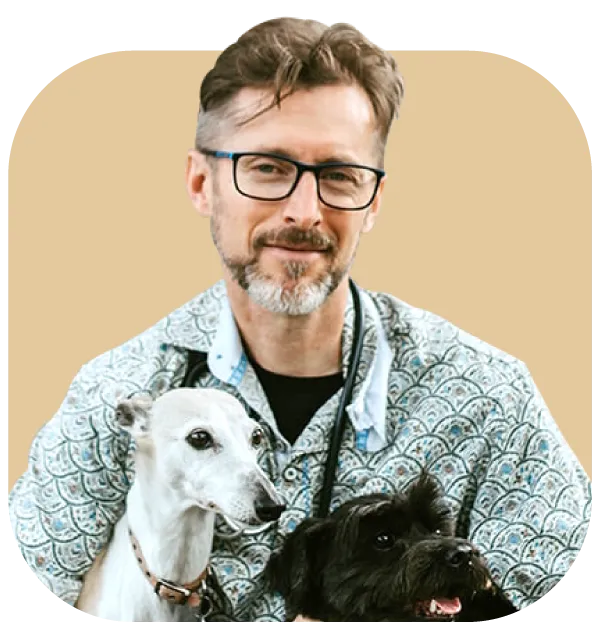 Holistic Veterinarian Dr Edward B smiles while holding a white dog and a black dog.