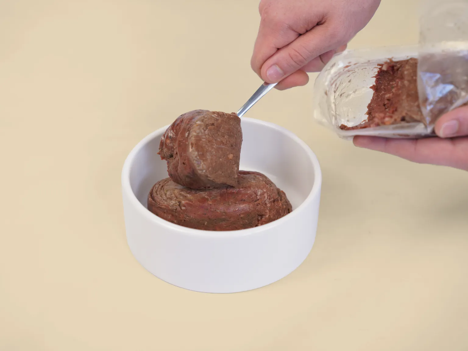 Hands spoon a patty of Kangaroo Low Allergy, Single Protein Raw Diet into a bowl.