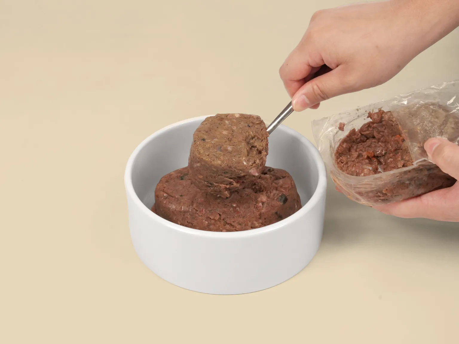 Hand spooning a patty of Tasmanian Salmon Raw Dog Food into a bowl.