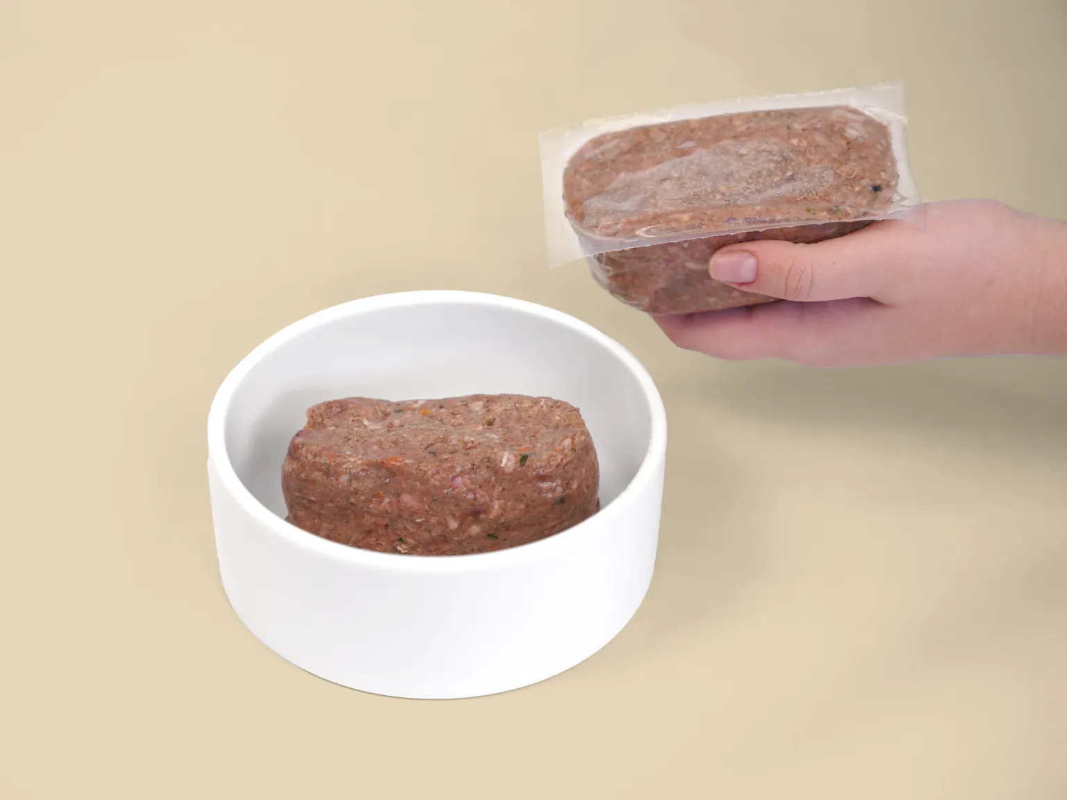A hand holds a patty of Combo Raw Dog Food over a bowl.
