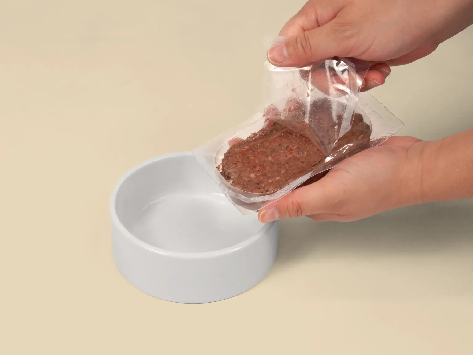 Hands opening a patty of Kangaroo Raw Cat Food over a bowl.