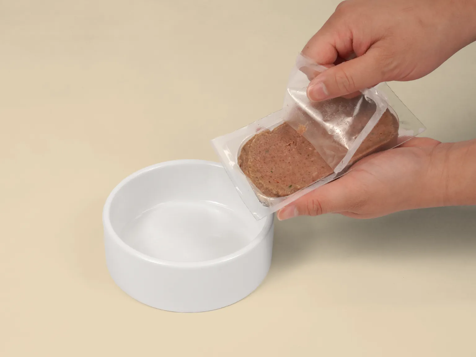 Hands opening a patty of Chicken Raw Cat Food over a bowl.