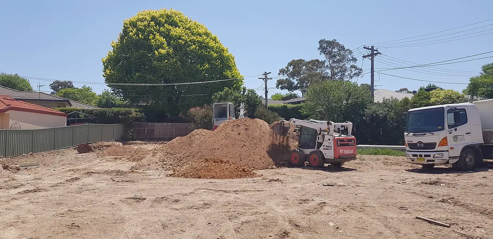 Construction site with a Bobcat loader moving a dirt pile and a white truck parked nearby.