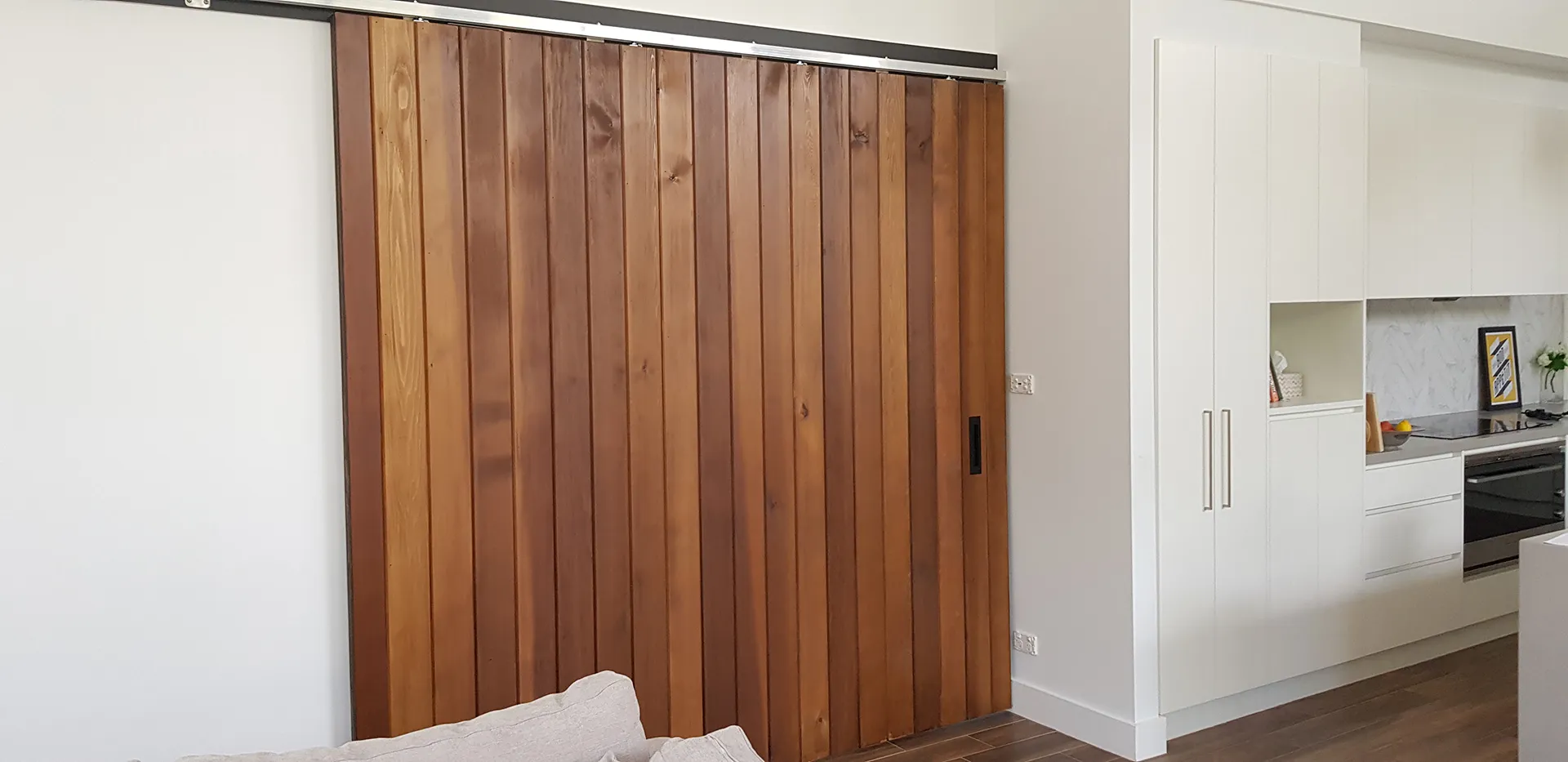 Wooden sliding door next to a modern white kitchen with stove and cabinets.