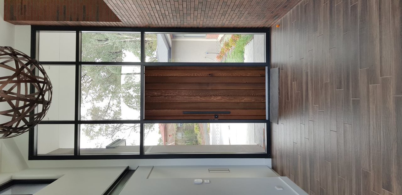 Entryway with tall wooden door framed by large glass panels and wood-look tile flooring.