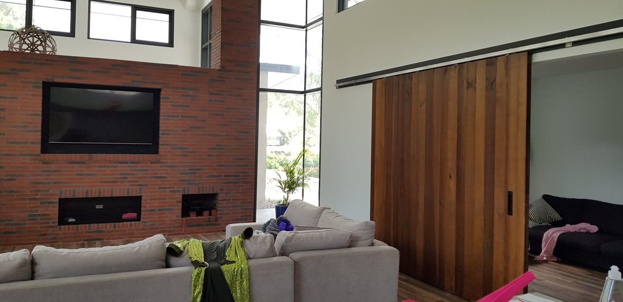 Modern living room with gray couches, brick wall with TV, large windows, and a wooden sliding door.