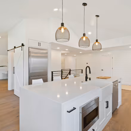 Modern white kitchen with a large island, black faucet, stainless steel appliances, and three pendant lights.