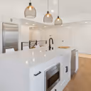Modern white kitchen with a large island, built-in sink, microwave, and three hanging pendant lights.
