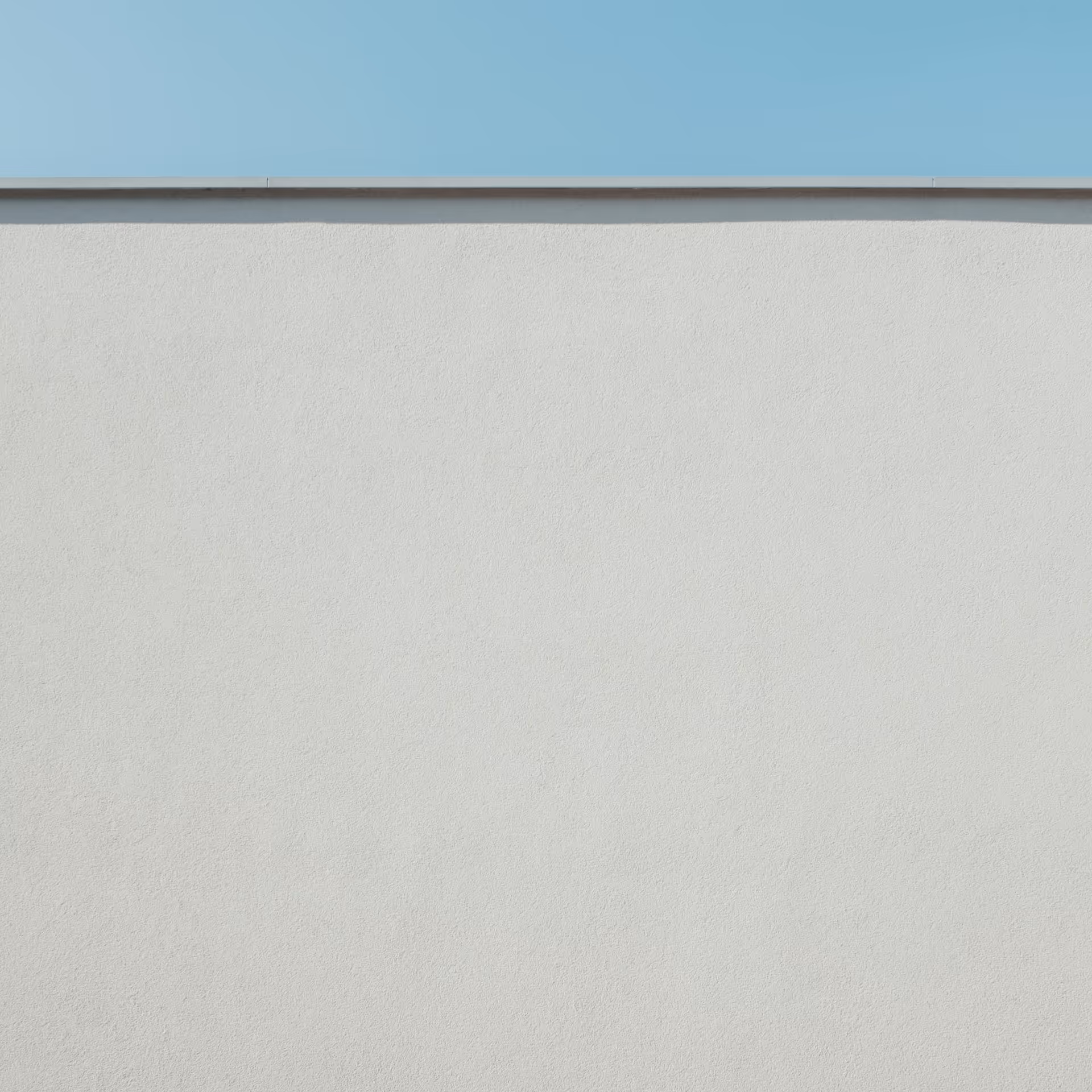 Smooth white concrete wall with a thin metal edge below a clear blue sky.