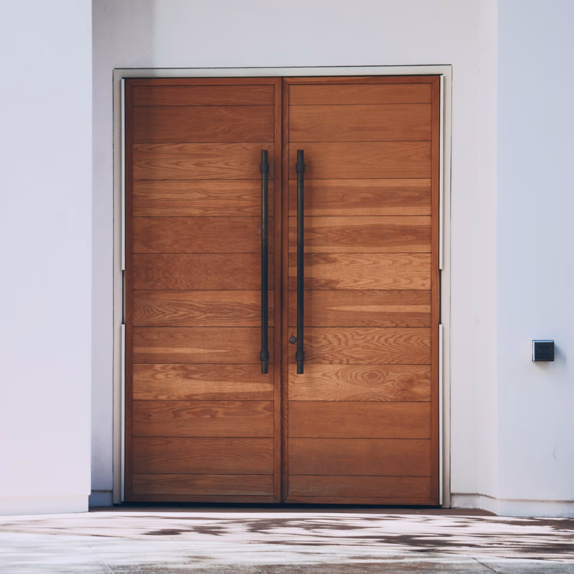 Double wooden front doors with horizontal panels and long black handles set in a white exterior wall.