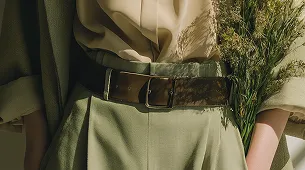  A close-up of a person wearing an earthy-toned outfit with a leather belt, set against a natural muted background.