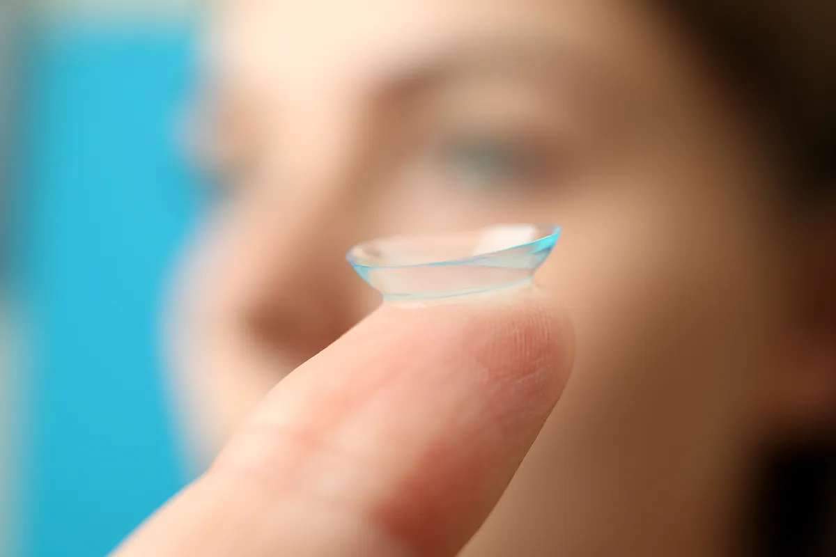 Close-up of a contact lens balanced on a fingertip with a blurred face in the background.