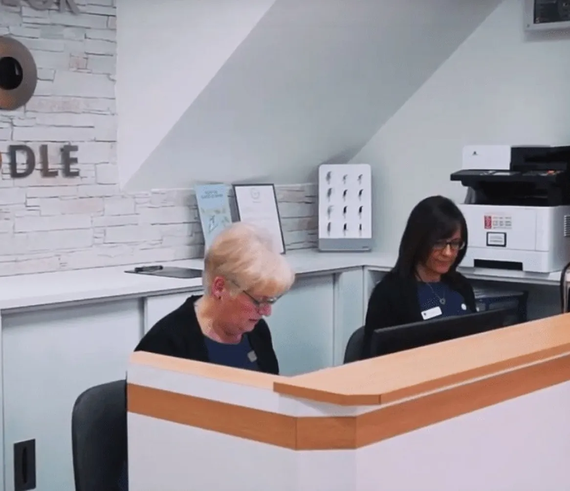 Two women sitting behind a reception desk, working on computers in a modern office.