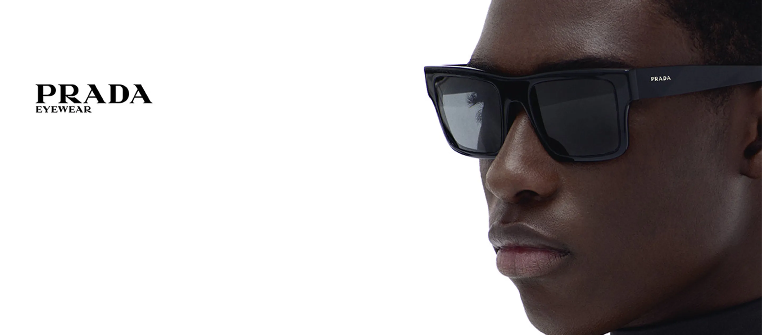Close-up of a person wearing black Prada sunglasses with PRADA Eyewear logo on the left temple.