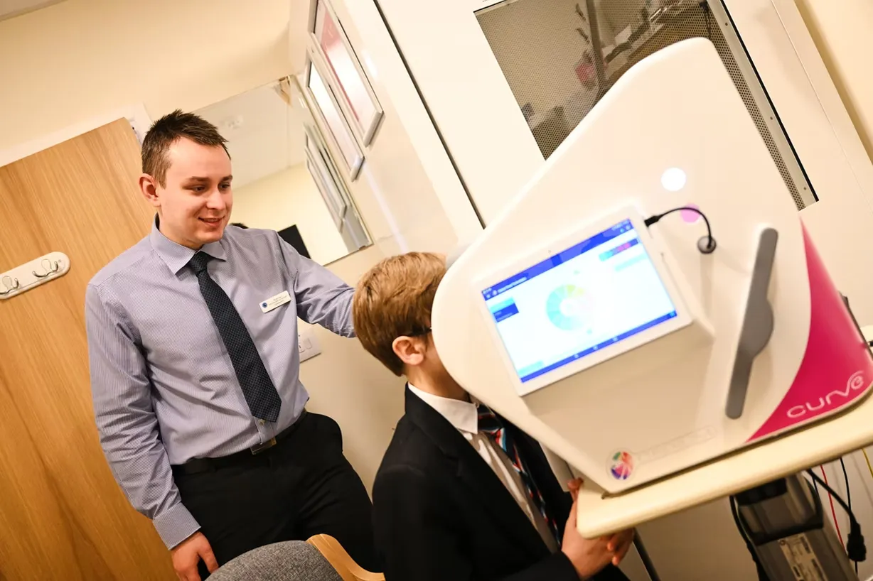 A man in a shirt and tie assists a boy in a suit vision testing with a machine displaying an eye diagram.