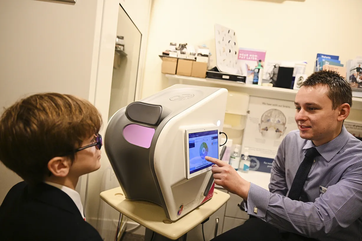 An eye care professional showing eye test results on a screen to a young patient wearing glasses during an eye exam.