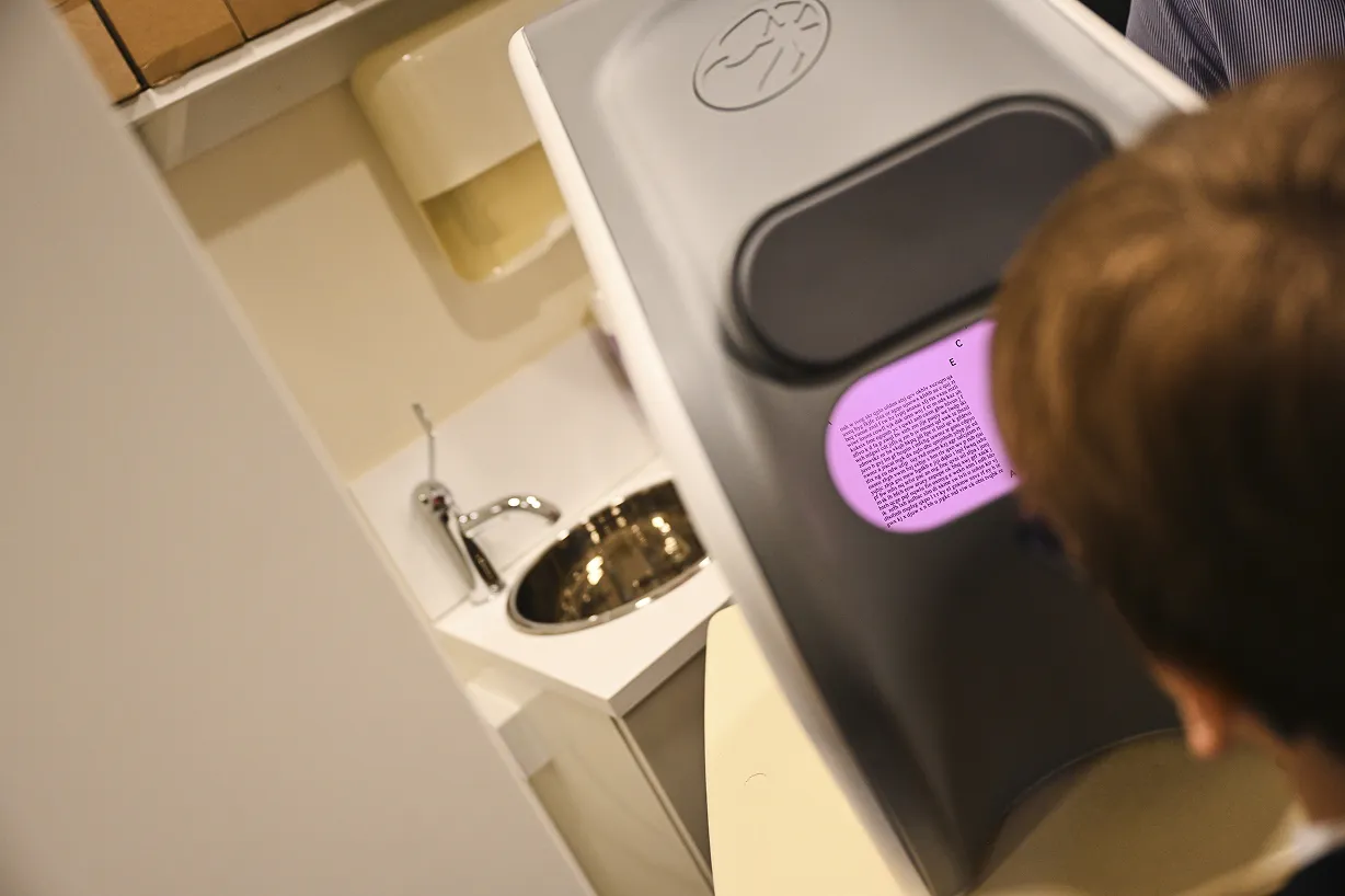 Child looking at a voting booth screen with a purple display in a bathroom-like room with a sink and towels.