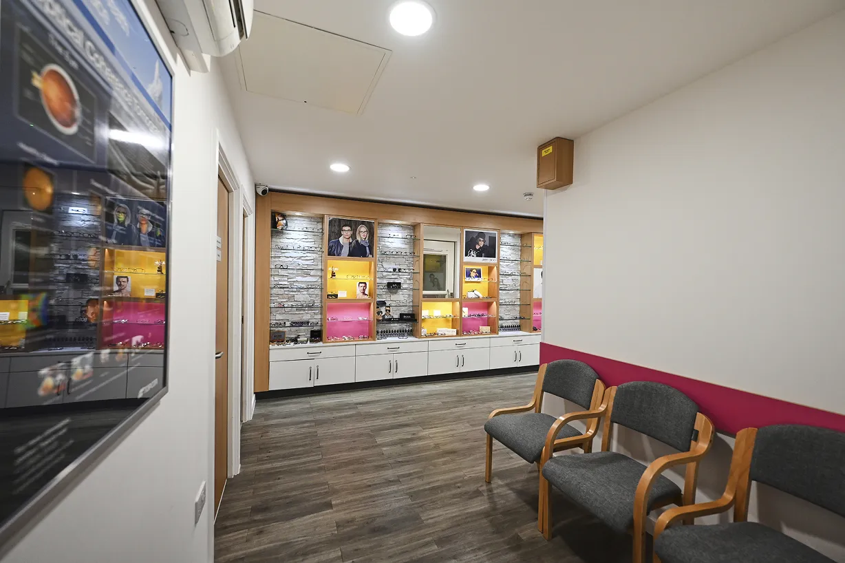 Modern optical shop interior with display shelves of eyeglasses and three gray chairs for waiting.