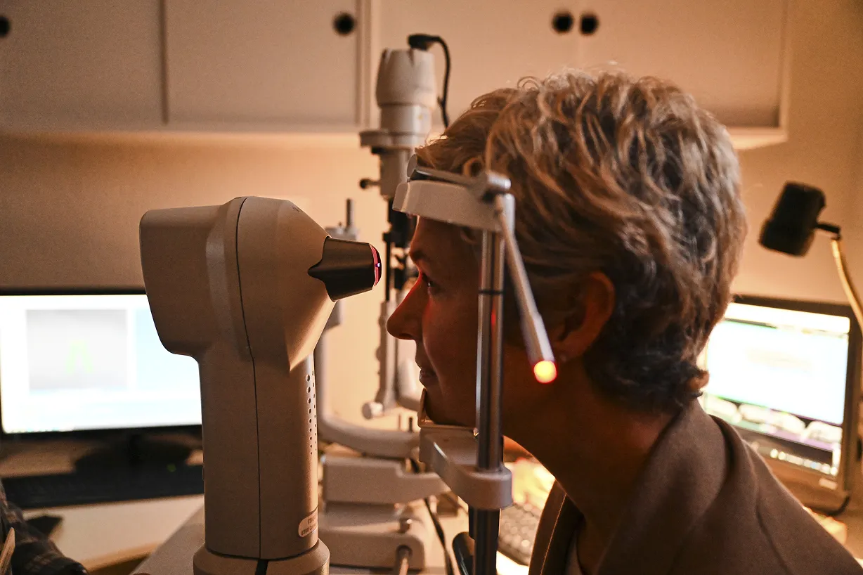 Woman undergoing an eye exam using a slit lamp in an ophthalmologist's office.