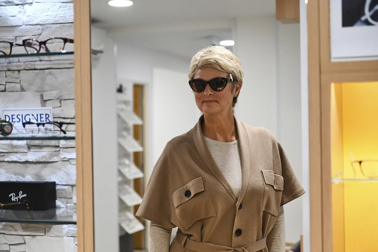 Woman with short blonde hair trying on black sunglasses in an eyeglass store.