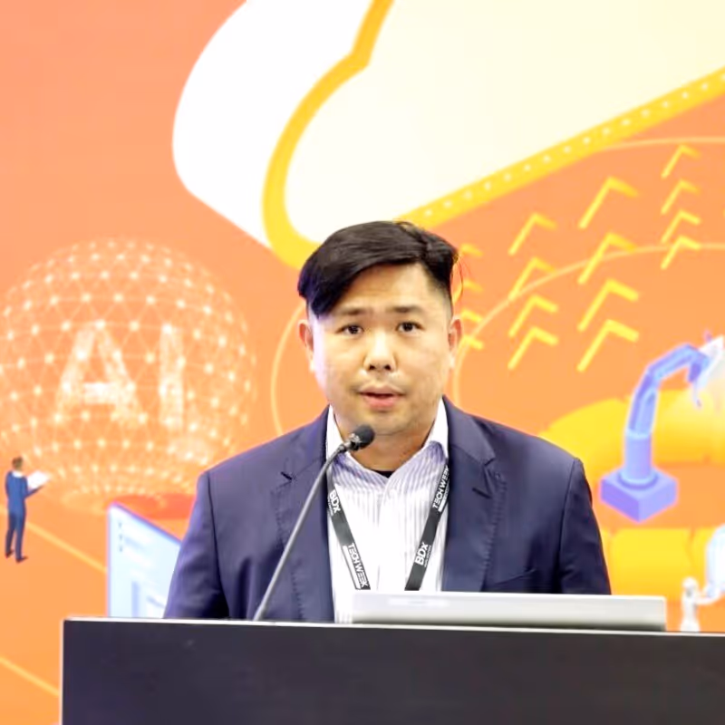 Smiling woman with dark hair tied in a bun wearing a black top against a plain light gray background.
