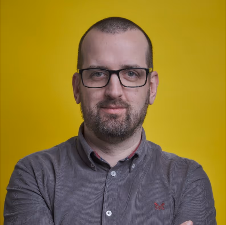 Smiling woman with dark hair tied in a bun wearing a black top against a plain light gray background.