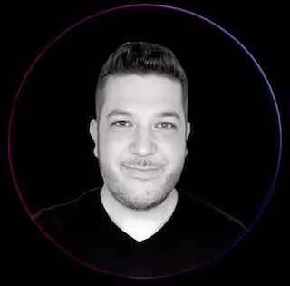 Smiling woman with dark hair tied in a bun wearing a black top against a plain light gray background.