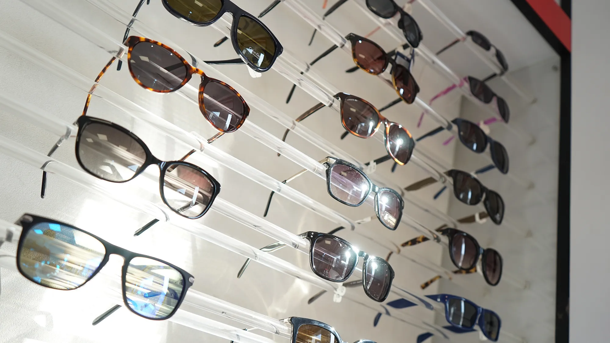 Multiple pairs of sunglasses displayed on clear horizontal rods against a wall.