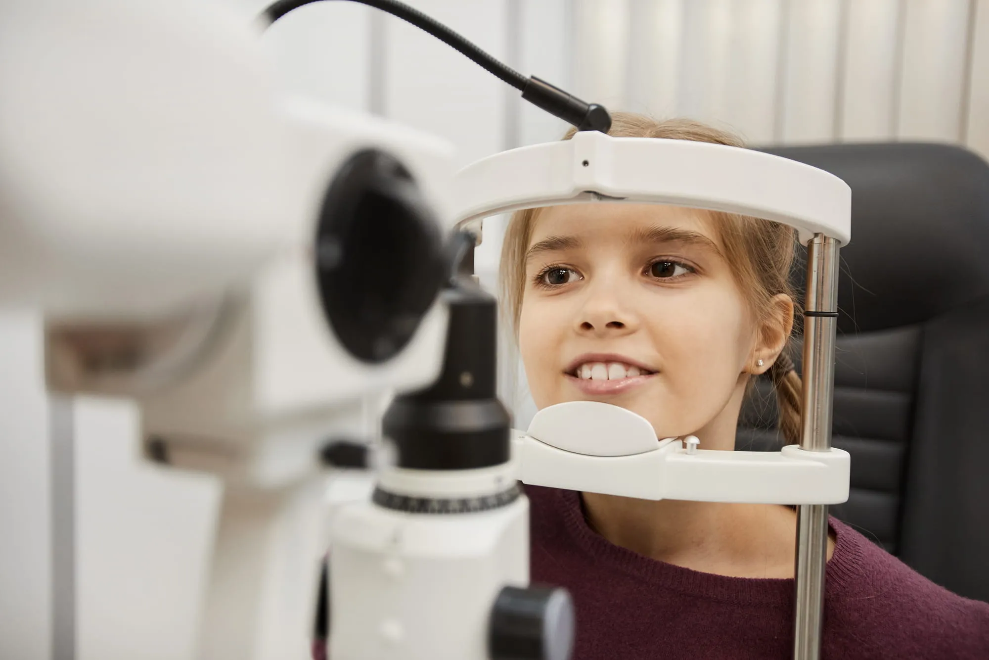 Young girl undergoing an eye examination using a slit lamp at the optometrist's office.