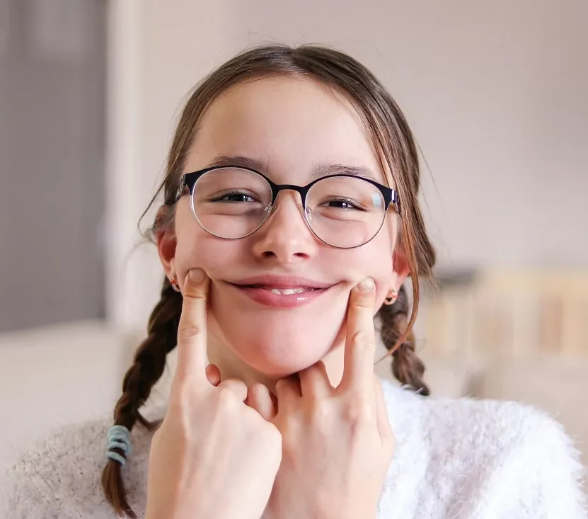 Girl with glasses and braided hair smiling while pressing her cheeks.