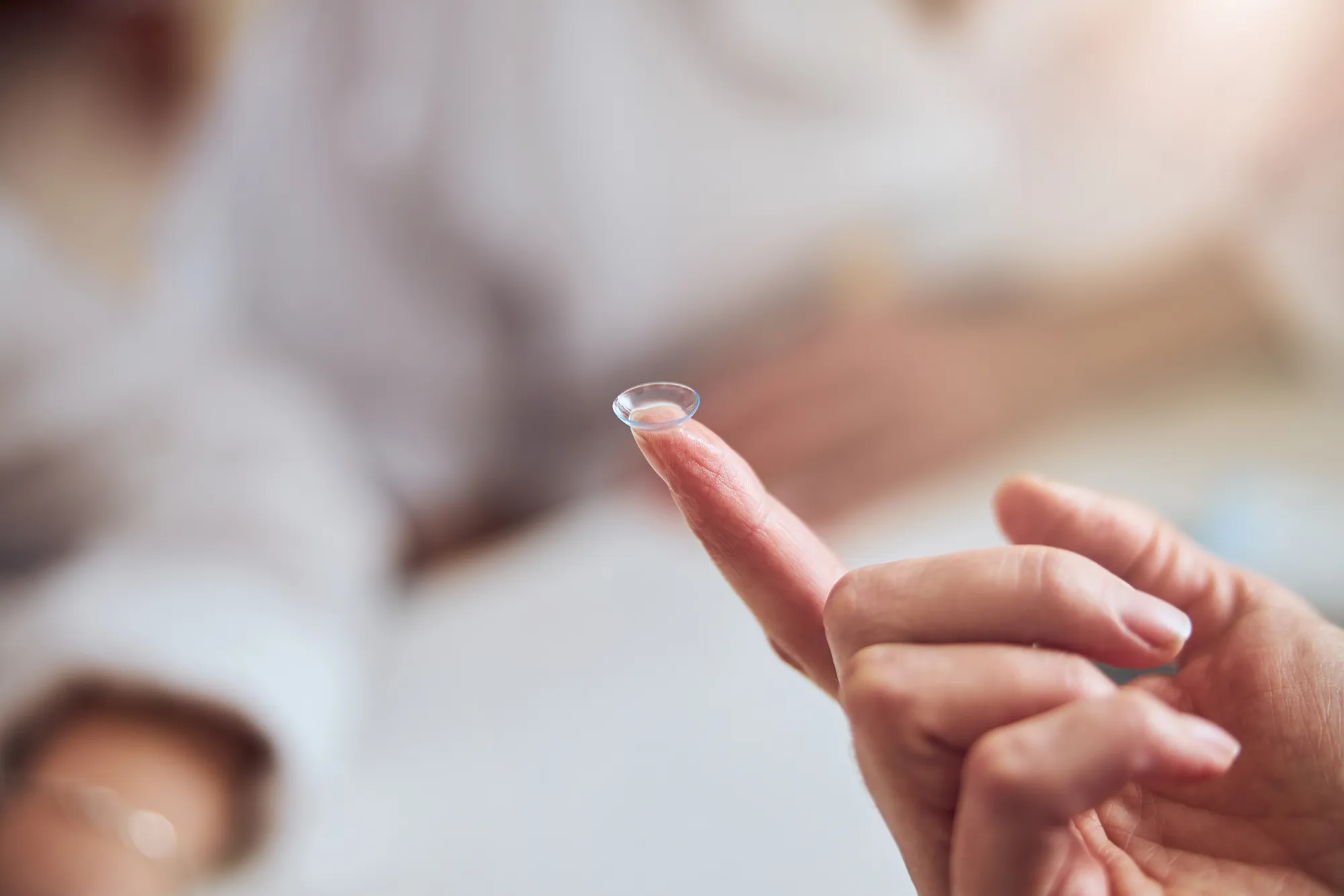 Close-up of a hand holding a transparent contact lens on the fingertip.