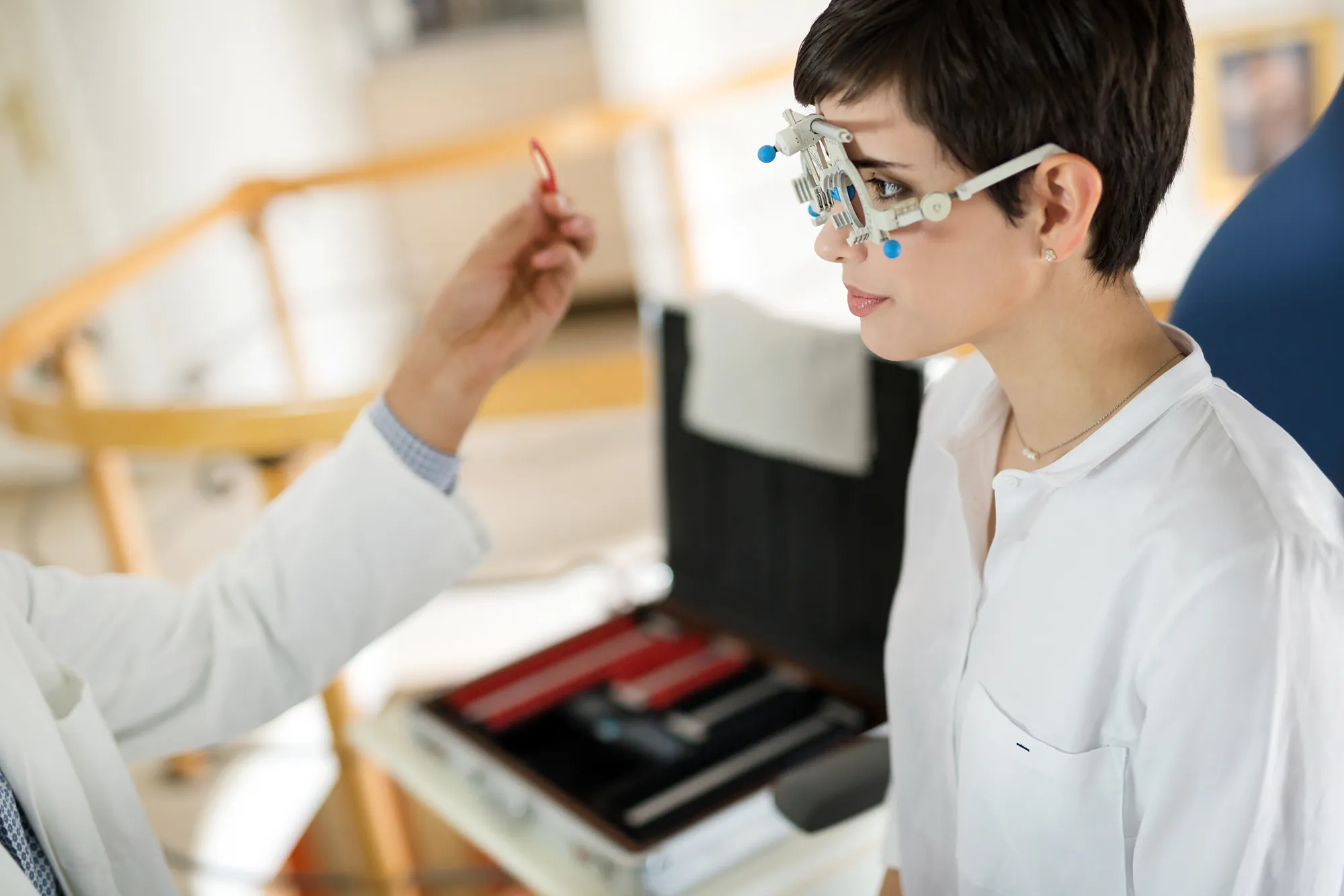Woman wearing a trial frame during an eye examination with an optometrist holding a lens.