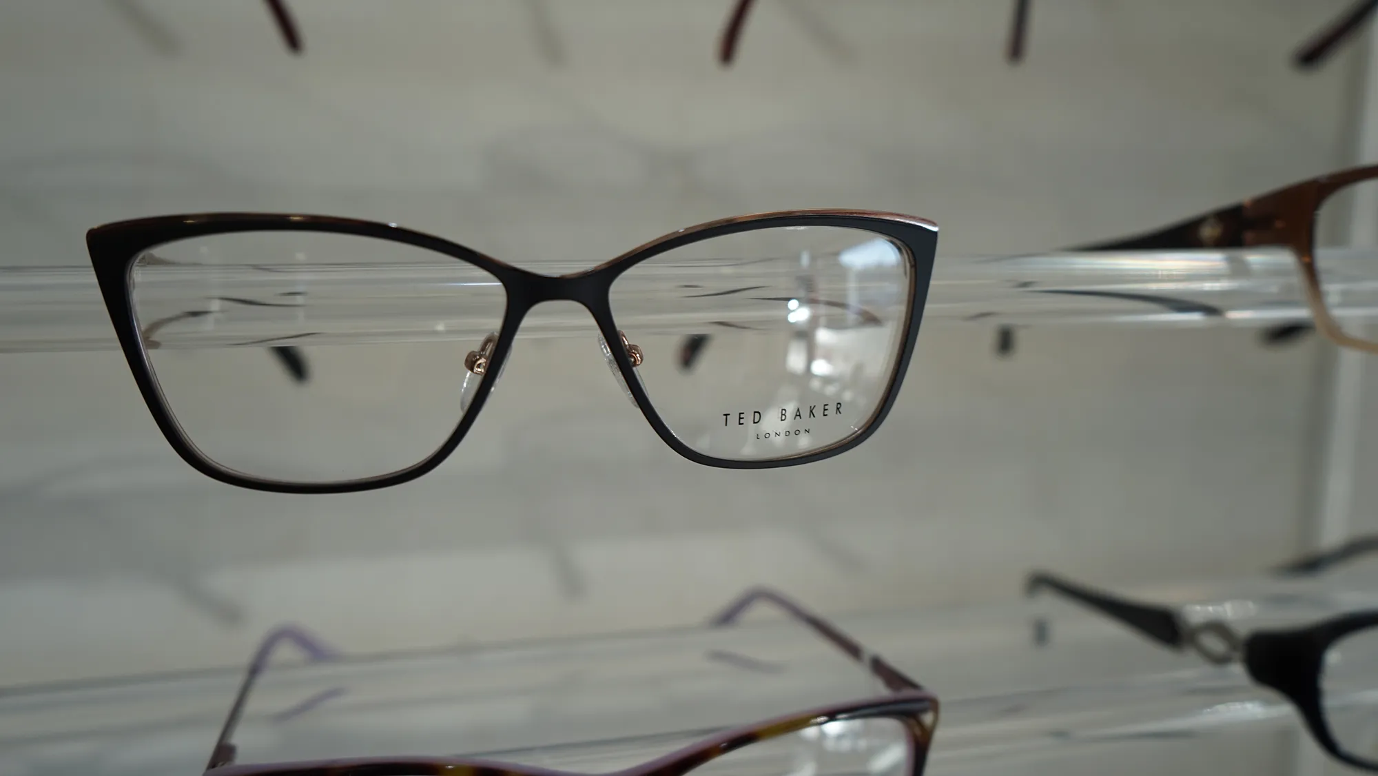 Close-up of black-rimmed Ted Baker London eyeglasses on a display rack.